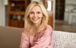 © Prostock-studio - Portrait Of Blonde European Mature Woman Posing Smiling To Camera Sitting On Sofa At Home. Lady Resting On Cozy Couch In Modern Living Room Indoor. Ageless Beauty And Elegance Concept