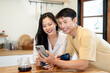 © bongkarn - Pretty asian woman and man couple looking at phone watching videos making coffee at kitchen counter.