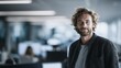 © 123sasha - Man with curly hair stands confidently in modern office setting while colleagues work at their desks during busy day