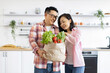 © sofiko14 - An Asian couple smiles while unpacking fresh produce from a paper bag in their bright, modern kitchen