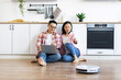 © sofiko14 - An Asian couple relaxes in their kitchen while a robot vacuum cleans the floor