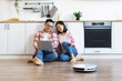 © sofiko14 - An Asian couple enjoys time together while their smart vacuum cleans the kitchen floor