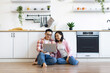 © sofiko14 - An Asian couple smiles while looking at a laptop computer in their modern kitchen