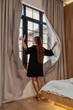 © svetograph - Woman curtains window opening morning light in a serene modern hotel bedroom