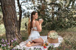© svetograph - Picnic Woman Tea: Summer morning, woman enjoys tea picnic in forest, relaxing with flowers and pastries outdoors.