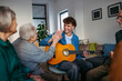 © Halfpoint - Young musician volunteer playing guitar for senirors in retirement home.