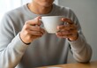 © Xisxas - Person holding a warm beverage in a ceramic mug while casually dressed in a sweater indoors near a window with natural light