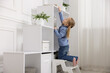 © New Africa - Child safety at home. Little girl on step ladder reaching for something on shelving unit indoors