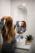 © Zoran Jesic - Woman brushing long hair in bathroom mirror