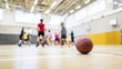 © Helga - junior basketball training captured during active drill, ball in controlled bounce near the floor, faceless children practicing across the court, modern school gym interior with sp