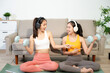 © Nuttapong punna - Two women exercising at home with dumbbells, yoga mat and headphones. Digital workout, fitness lifestyle, wellness and healthy living