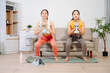 © Nuttapong punna - Two women exercising at home with dumbbells, yoga mat and headphones. Digital workout, fitness lifestyle, wellness and healthy living with online training concept.