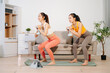 © Nuttapong punna - Two women exercising at home with dumbbells, yoga mat and headphones. Digital workout, fitness lifestyle, wellness and healthy living with online training concept.