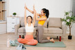 © Nuttapong punna - Two women practicing yoga at home with a personal trainer. Indoor fitness workout, stretching and wellness lifestyle using online guidance