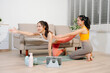 © Nuttapong punna - Two women practicing yoga at home with a personal trainer. Indoor fitness workout, stretching and wellness lifestyle using online guidance