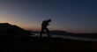 © banphote - Silhouette of a hiker walking on a hill at dusk with a calm evening sky.