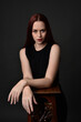 © faestock - close up portrait of beautiful female model with long red hair and black shirt, gestural hand and arm poses, leaning on wooden plinth. classic studio portrait on dark background.