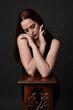 © faestock - close up portrait of beautiful female model with long red hair and black shirt, gestural hand and arm poses, leaning on wooden plinth. classic studio portrait on dark background.