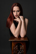 © faestock - close up portrait of beautiful female model with long red hair and black shirt, gestural hand and arm poses, leaning on wooden plinth. classic studio portrait on dark background.