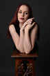 © faestock - close up portrait of beautiful female model with long red hair and black shirt, gestural hand and arm poses, leaning on wooden plinth. classic studio portrait on dark background.