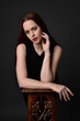 © faestock - close up portrait of beautiful female model with long red hair and black shirt, gestural hand and arm poses, leaning on wooden plinth. classic studio portrait on dark background.