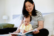 © NZstockphoto - Asian mum reading a book to toddler daughter in bed