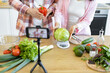 © sofiko14 - A couple prepares a cooking video with fresh vegetables on a wooden table in a well-lit kitchen