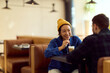 © bnenin - Asian Woman in Yellow Beanie Enjoying Coffee Chat With Friend in Cozy Cafe Sitting Together