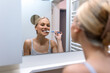 © Graphicroyalty - Woman Brushing Teeth in Bathroom Mirror. Dental hygiene and oral care concept, People with daily health routine. Attractive woman smiling and cleaning teeth with toothbrush in front of mirror.