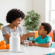 © Yuliya - Caring mother gives her child a vitamin supplement at home. A happy boy takes vitamins from a spoon at the table. Concept of children’s health, immunity, proper nutrition, family care, and prevention.