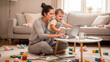 © Margo Miro - Mother multitasking with a toddler while working on a laptop in a cozy living room