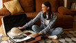 © Home-stock - Happy woman packing suitcase with clothes, map, hat and documents, sitting on floor in living room, panorama shot. Travel preparation concept