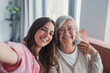 © Daniel - Smiling middle aged mother and daughter taking selfie together, hugging and sitting on couch at home, young woman and happy older mature mum photographing, two generations good relations