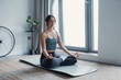 © Daniel - Young sporty attractive woman practicing yoga, doing Ardha Padmasana exercise, Half Lotus pose with mudra, working out, wearing sportswear, grey pants, top, indoor full length, yoga studio, side view