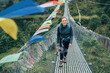 © Soloviova Liudmyla - Young smiling female hiker woman crossing canyon over Suspension Bridge decorated with multicolored Tibetan Prayer flags hinged over gorge. Everest Base Camp route, Sagarmatha National Park, Nepal.