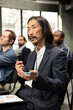 © DC Studio - Asian man in attendance talking on microphone and interacting with speaker at business event, asking questions during presentation. International summit focuses on development.