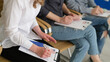 © H_Ko - In a contemporary office space, several individuals are seated, intently writing notes on clipboards.