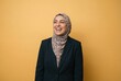 © Stitch - A cheerful Muslim businesswoman in a hijab and suit laughing heartily on a yellow background.