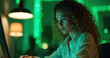 © Maryna - Young woman works on laptop at night. Neon green lights illuminate desk. Person types on computer keyboard with focus. Home office setting with desk lamp.