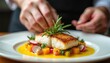 © Maryna - Chef garnishes pan seared fish fillet with rosemary herb. Meal includes diced pumpkin radish atop bright yellow sauce. Professional plating creates beautiful appetising presentation for diner.