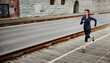 © BuyoutReese08/peopleimages.com - Exercise, woman and running with earphones in city for speed training, fitness playlist or cardio. Space, athlete and music outdoor for jogging routine, health challenge and streaming workout podcast