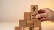 © Rahman - Hand placing wooden block with plant icon onto a growing stack of blocks symbolizing business growth, sustainability, investment, and career development