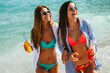© NDABCREATIVITY - Two happy women toasting colorful beach drinks under the sun, enjoying tropical vibes and friendship