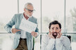 © deagreez - Deadline pressure at the office as a tired businessman sits at his desk while a colleague holds a deadline sign