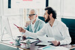© deagreez - Business meeting in modern office two colleagues discuss documents and strategy at a sleek desk while one man points at a computer screen for a productive corporate discussion