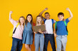 © Anastasiya - Cheerful group of preteen children with laptop celebrating success with raised arms on yellow studio background. Positive emotions, teamwork, school achievement, and education concept