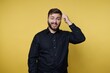 © bodnarphoto - Man with beard smiles and scratches his head in front of a yellow background during a casual moment