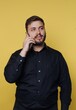 © bodnarphoto - Man talks on a phone with a smile while standing in front of a yellow background during daytime