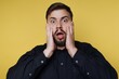© bodnarphoto - Surprised man shows shock with hands on face in front of yellow background during daytime in a studio setting