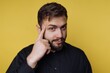 © bodnarphoto - Man with beard thinks while touching his temple against a bright yellow background in a studio setting